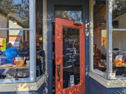 A cozy restaurant entrance with a bright orange door and a sign indicating hours of operation.