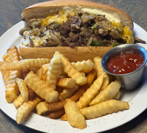 A loaded cheesesteak sandwich with peppers and melted cheese, served with a side of crinkle-cut fries and ketchup.