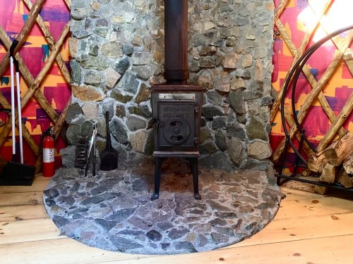 A rustic stone fireplace with a metal stove, surrounded by colorful walls and wooden flooring.