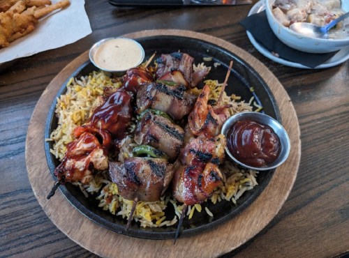 A sizzling platter of skewered meats on a bed of rice, accompanied by dipping sauces.