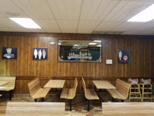 Interior of an ice cream shop with wooden walls, empty tables, and framed ice cream art on the wall.