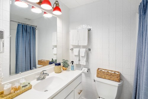 Bright bathroom with white tiles, a mirror, blue curtains, and neatly arranged towels and toiletries.