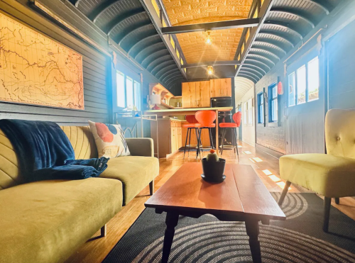 Cozy interior of a stylish tiny home with a sofa, chairs, wooden table, and modern kitchen in the background.