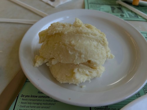 A small mound of mashed potatoes on a white plate, set on a table with menus in the background.
