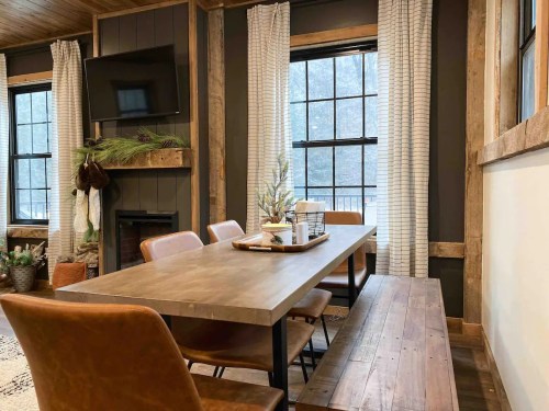 A cozy dining area with a wooden table, leather chairs, and large windows, featuring rustic decor and a warm atmosphere.