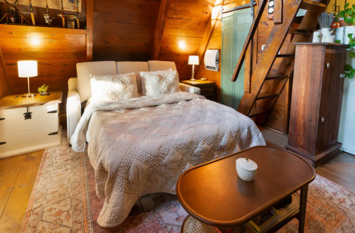 Cozy attic bedroom with a double bed, wooden walls, a coffee table, and a staircase leading to another level.