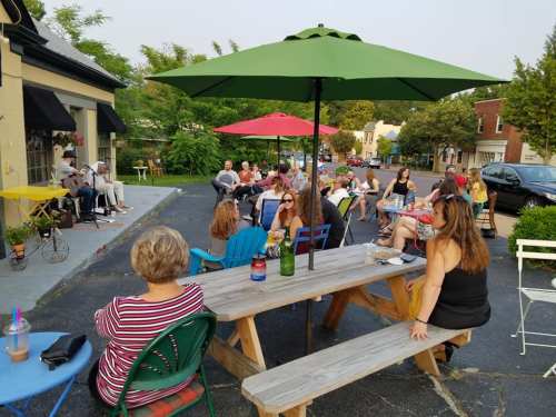 A lively outdoor gathering with people seated at tables under colorful umbrellas, enjoying a sunny day.