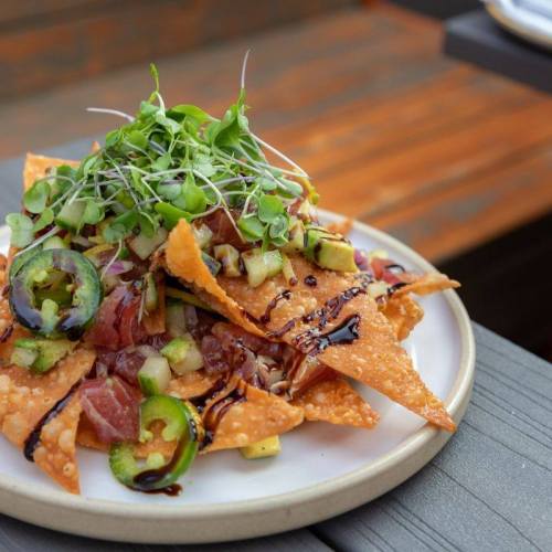 A plate of crispy nachos topped with diced vegetables, jalapeños, and microgreens drizzled with sauce.