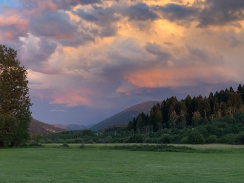 A scenic landscape featuring rolling hills, lush greenery, and a colorful sunset sky with clouds.