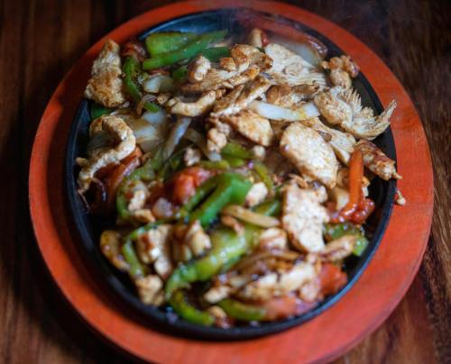 Sizzling fajitas with grilled chicken, bell peppers, and onions on a wooden platter, emitting steam.