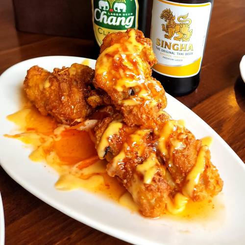 Crispy fried chicken wings drizzled with sauce, served on a white plate alongside bottles of Chang and Singha beer.