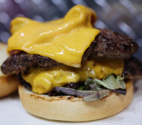 Close-up of a juicy cheeseburger with two beef patties, melted cheese, and fresh greens on a toasted bun.