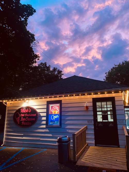 A charming ice cream parlor with a neon "Open" sign, set against a colorful sunset sky.