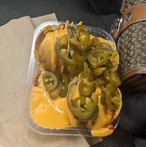 A plastic container filled with nachos topped with melted cheese and sliced jalapeños, resting on a napkin.
