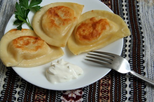 Three golden-brown dumplings on a plate with a dollop of sour cream, garnished with parsley, on a patterned tablecloth.