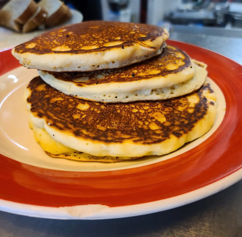 Three golden-brown pancakes stacked on a red and white plate, with a soft texture and crispy edges.