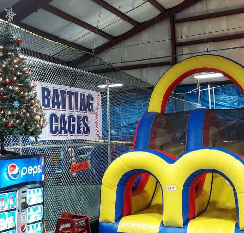 Indoor batting cages with a festive Christmas tree and a colorful inflatable slide nearby.