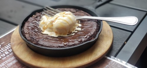 A warm chocolate brownie in a skillet topped with vanilla ice cream and drizzled with caramel sauce.