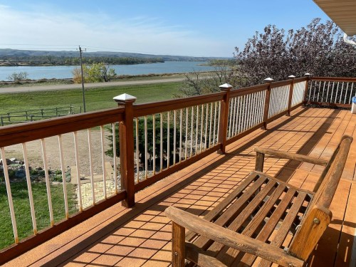 A wooden deck with a bench overlooks a river and green fields under a clear blue sky.
