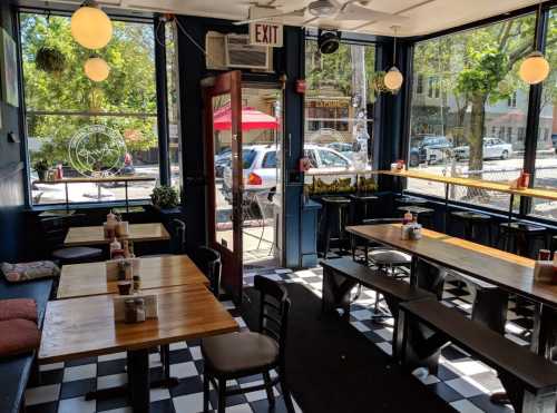 Cozy café interior with wooden tables, black and white checkered floor, and large windows letting in natural light.