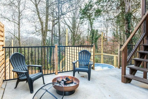 A cozy outdoor space with two chairs, a fire pit, and a hot tub, surrounded by trees and a wooden railing.