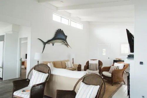 Bright, airy living room with a large fish mounted on the wall, featuring wicker chairs and a cozy sofa.