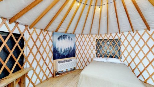 Cozy interior of a yurt with wooden lattice walls, a bed, and a decorative wall hanging.