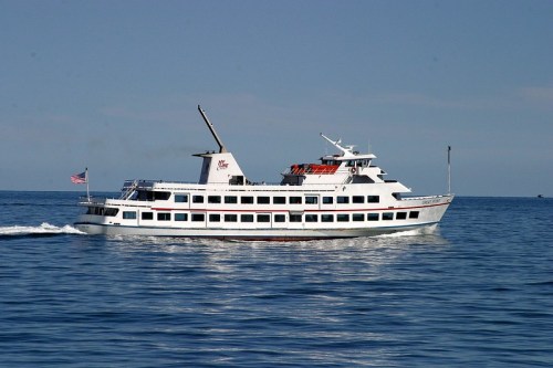 A white passenger boat with an American flag sails on calm blue waters under a clear sky.