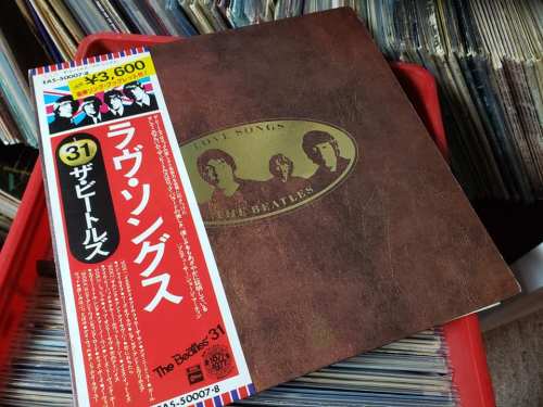 A vintage Beatles album titled "Love Songs" with a Japanese price tag, surrounded by other records in a crate.