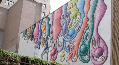 Colorful mural featuring whimsical, cartoonish faces with exaggerated expressions on a building wall.