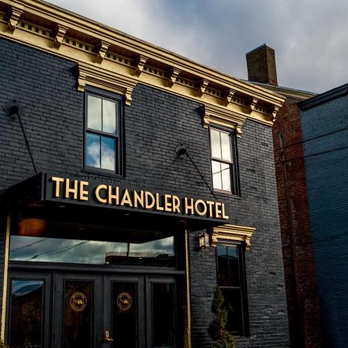 Exterior of The Chandler Hotel, featuring a black brick facade and gold lettering against a cloudy sky.