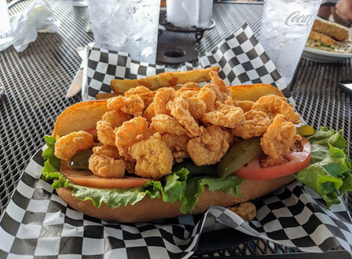 A large sandwich filled with crispy fried shrimp, lettuce, tomato, and pickles, served on a checkered plate.