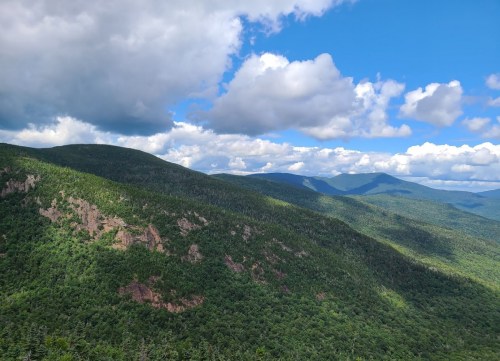 A panoramic view of lush green mountains under a partly cloudy blue sky.