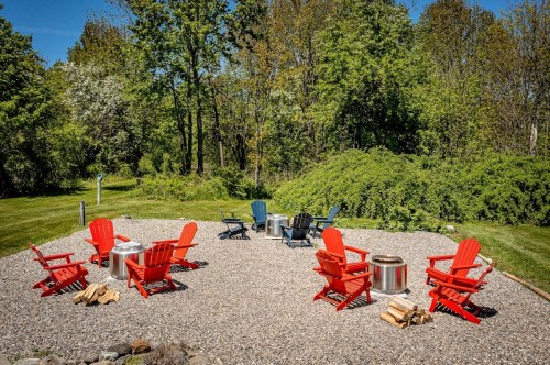 A cozy outdoor seating area with red and blue chairs, fire pits, and a gravel surface surrounded by greenery.