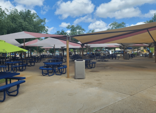 A spacious outdoor area with blue picnic tables under colorful canopies and a clear blue sky.
