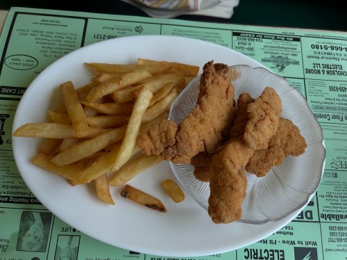 A plate with crispy fried chicken tenders and a side of golden French fries on a green menu background.