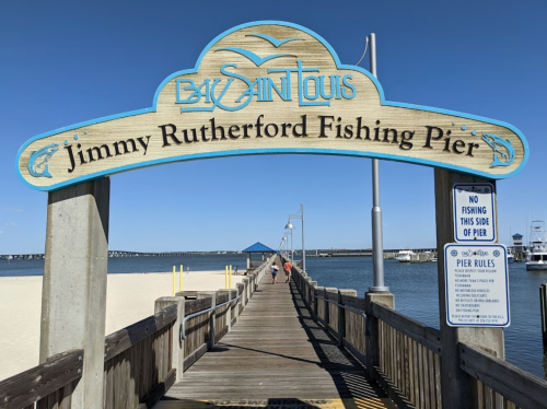 Sign for Jimmy Rutherford Fishing Pier, leading to a wooden walkway over water with boats in the background.
