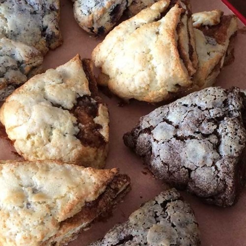 A close-up of freshly baked scones in various flavors, including chocolate and cinnamon, arranged on parchment paper.