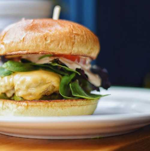 A close-up of a delicious burger with a soft bun, lettuce, tomato, and melted cheese on a white plate.