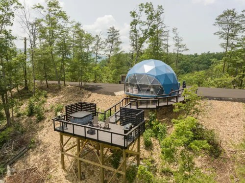 A modern blue geodesic dome on a wooden deck, surrounded by trees and a scenic landscape.