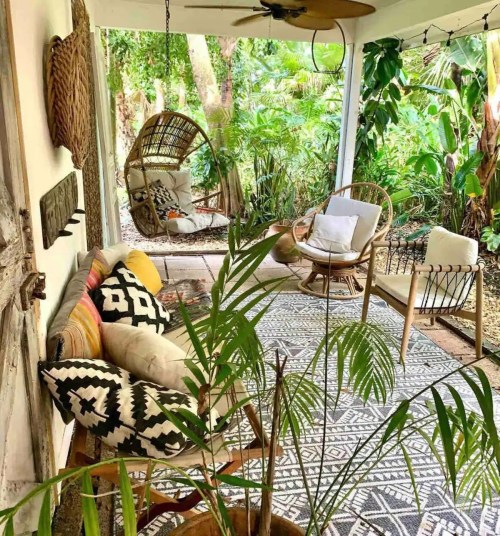 Cozy outdoor seating area with hanging chairs, patterned rug, and lush greenery in a tropical setting.