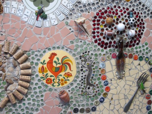 Colorful mosaic featuring a rooster design, various sports balls, bottle caps, and decorative objects.