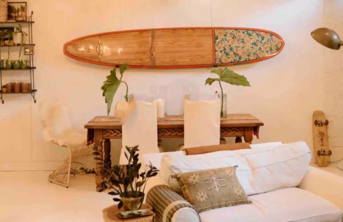 A cozy living space featuring a wooden table, surfboard art, and a white sofa with decorative pillows.