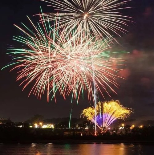 Colorful fireworks burst in the night sky over a dark landscape, creating a vibrant display of light and color.