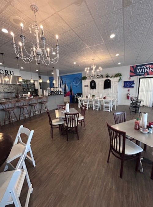 Interior of a cozy restaurant with wooden tables, chairs, chandeliers, and a mural on the wall.