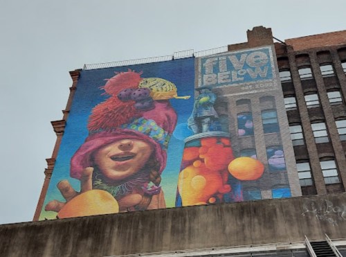 Colorful mural on a building featuring a playful character with vibrant accessories and whimsical elements.