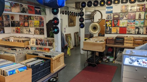 A cozy record store with shelves of vinyl records, vintage decor, and a large gramophone on display.