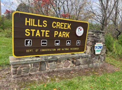 Sign for Hills Creek State Park, featuring icons for activities and information about conservation and natural resources.
