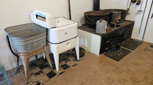 A vintage laundry setup featuring a wash basin, a washing machine, and a large stove in a rustic kitchen.