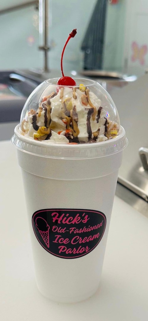 A cup of ice cream topped with whipped cream, nuts, chocolate drizzle, and a cherry, from Hick's Old-Fashioned Ice Cream Parlor.